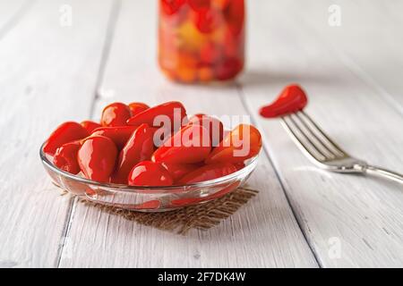 Eingelegte rote Paprika auf einer Glasuntertasse über einem weißen Holztisch. Marinierte Paprika-Schoten aus nächster Nähe. Fermentiertes Bio-Gemüse. Stockfoto