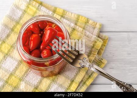 Eingelegter Baby Red Hot Pepper auf einer Gabel über offenem Glas auf einem weißen Holztisch. Marinierte Paprika-Schoten. Fermentiertes Bio-Gemüse. Stockfoto