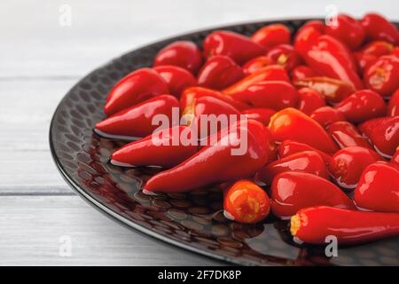 Nahaufnahme von eingelegten roten Paprika auf einem schwarzen Teller. Marinierte Paprika-Schoten aus nächster Nähe. Fermentierte Bio-Gemüsesnacks. Stockfoto