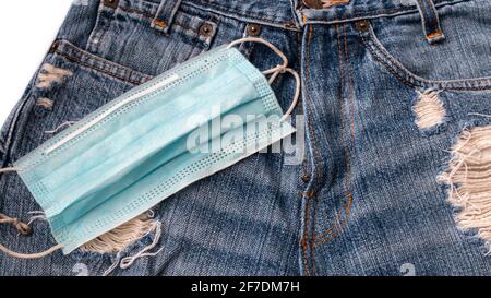 Eine OP-Maske, die im Februar 2021, einem Jahr nach der COVID-19-Pandemie, auf einem Paar beklemmter blauer jean-Shorts aufliegt. Stockfoto