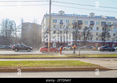 Moskau. Russland. 06. April 2021. Orangefarbene uniformierte Hausmeister, die auf einer Straße in der Stadt den Rasen fegen. Sonniger Frühlingstag. Die Arbeit der Gemeinde Stockfoto