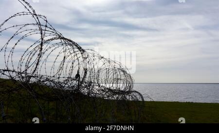 Nahaufnahme eines alten Stacheldrahtes aus Metall aus dem zweiten Weltkrieg. Scharfer Stacheldrahtzaun in der Nähe des Meeres während des Sonnenuntergangs. Konzept von Gefängnis oder Einwanderung Stockfoto