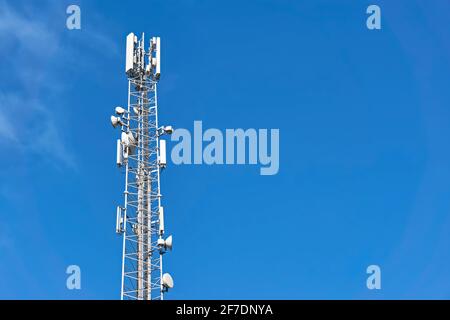 4G- und 5G-Sender auf einem Telekommunikationsturm. Mobilfunkbasisstation mit weißen Sendeantennen auf einem hohen Pol gegen einen blauen Himmel. Stockfoto