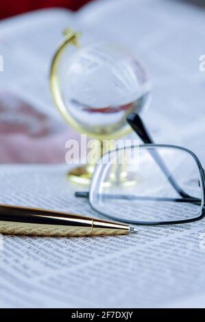 Brille, Stift, Globus liegen auf einer Zeitung Stockfoto