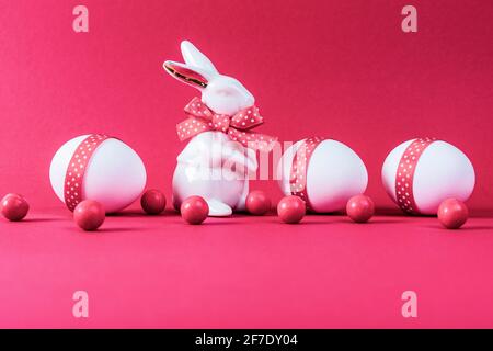 Osterkonzept. Porzellan Kaninchen mit drei weißen Eiern mit rosa Band auf rosa Papier Hintergrund verziert. Speicherplatz kopieren. Stockfoto