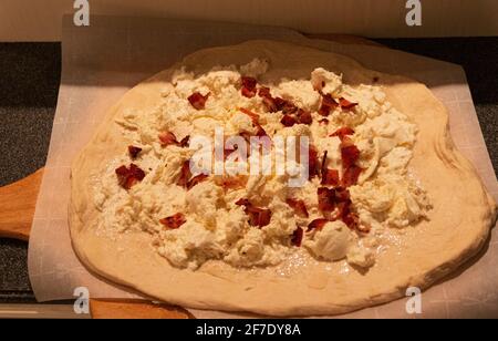 Eine hausgemachte weiße Pizza mit Ricotta-Käse und Speck steht auf dem Pizzabrett und kann zum Backen in den Ofen gestellt werden. Stockfoto