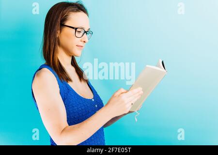 Schöne junge Frau liest ein Buch im Profil mit Brille auf blauem Hintergrund. Gemeinsam lesen Konzept Freizeit Konzept Stockfoto