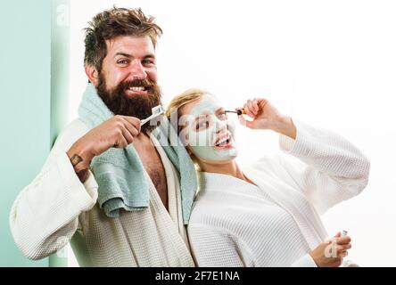 Morgenbehandlungen. Paar im Bad. Mann und Frau. Ehemann mit Zahnbürste, Ehefrau mit kosmetischer Gesichtsmaske. Stockfoto