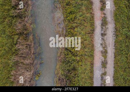 Luftaufnahme des weißen trüben Baches und der Schotterstraße daneben. Auf dem Kopf stehendes Foto eines Flusses und Pfades am trüben grauen Herbsttag. Stockfoto