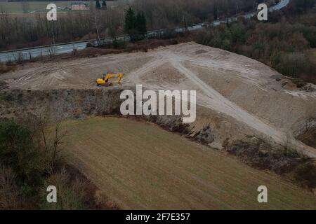 Ein gelber Bagger oder Bagger steht an einem bewölkten Tag in einer Sandgrube oder Kiesgrube neben einer Landstraße. Stockfoto