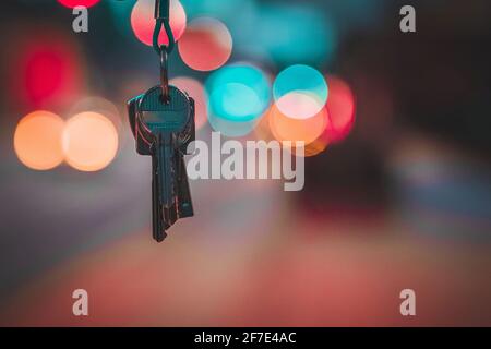 Ein Satz moderner Metallschlüssel, die von oben hängen, mit einem verschwommenen Hintergrund aus roten und blauen Lichtern. Tasten auf unscharfem Bokeh-Hintergrund. Foto des Konzeptschlüssels Stockfoto