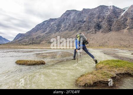 Backpacker nutzt Trekkingstöcke, um über einen tiefen Fluss zu springen Kanal Stockfoto