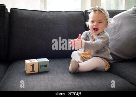 Ein Jahr altes Mädchen sitzt auf der Couch und klatscht vor Aufregung Stockfoto