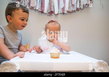 Bruder hilft seiner einjährigen Schwester zuerst bei ihr Geburtstag Stockfoto