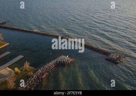 Gezeitenbarriere um einen kleinen Yachthafen. Breakwater Barriere aus Steinen, um einen sicheren Hafen für Schiffe oder Boote zu schaffen. Stockfoto