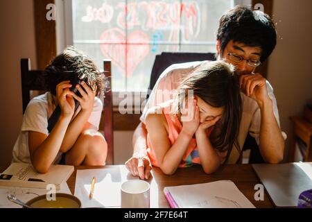 Zwei unglückliche Kinder mit Kopf in den Händen sitzen müde Vater am Tisch Stockfoto