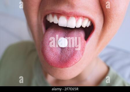 Junge Frau nimmt die Kapsel ein. Nahaufnahme der weißen runden Pille auf der Zunge. Tablette mit offenem Mund halten Stockfoto