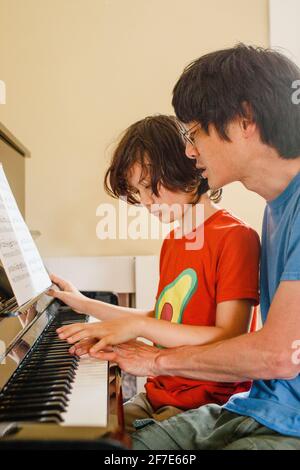 Ein Vater und ein Sohn sitzen beim Klavierbau eng beieinander Musik Stockfoto