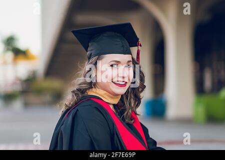 Lächelnde Frau, die das College abschloss, trägt einen Abschlusskleid/Mütze. Stockfoto