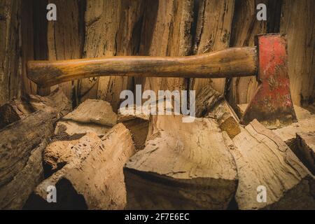 Die Beil-Axt steckt in einem Stapel gespaltener Holzstämme, die zum Feuer verwendet werden. Konzept der Herstellung von Baumstämmen mit natürlichen Farben- Axt von der Seite gesehen. Stockfoto