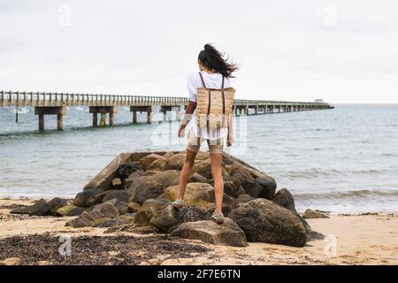 Junge Frau, die an bewölktem Tag einen felsigen Strand erkundet Stockfoto