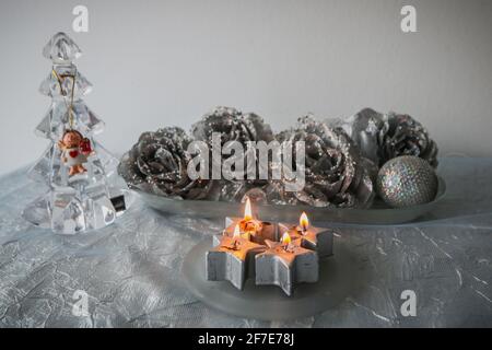 Schöne weihnachtsschmuck in silberner Farbe und Glas auf einem Tisch angeordnet. Es werden vier sternförmige Kerzen angezündet. Stockfoto