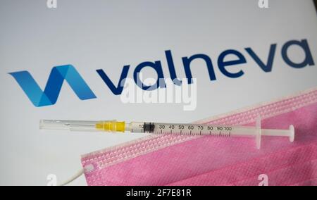 Valneva COVID-19 Impfstoffkonzept. Spritze, Gesichtsmaske und Valneva Firmenlogo auf dem unscharfen Hintergrundbildschirm. Stafford, Großbritannien, 6. April 202 Stockfoto