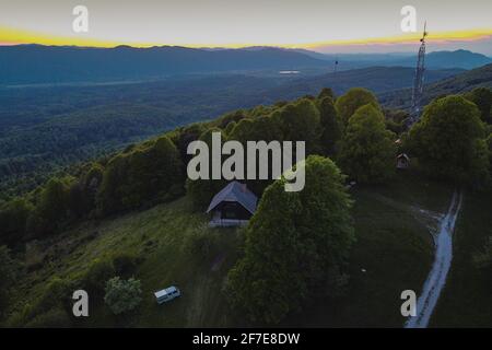 Wildes Campen mit einem Kleinbus in der Region Kocevsko in Slowenien bei Sonnenuntergang oder am Abend. Schönes Panorama der Hügel rund um Kocevje mit Berghütte und Stockfoto