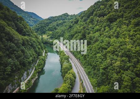 Panorama eines engen Flusstals mit einer engen Eisenbahnlinie und einer Straße neben einem breiten grünen Fluss Sava in der Nähe von Hrastnik und Trbovlje. Stockfoto