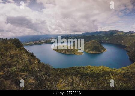 Blick auf die Insel am berühmten Cuicocha-See in Ecuador. Panorama über einen blauen See, umgeben von üppigem Grün und weißen Wolken. Stockfoto