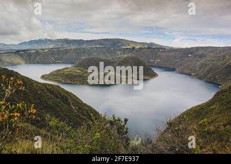 Blick auf die Insel am berühmten Cuicocha-See in Ecuador. Panorama über einen blauen See, umgeben von üppigem Grün und weißen Wolken. Stockfoto