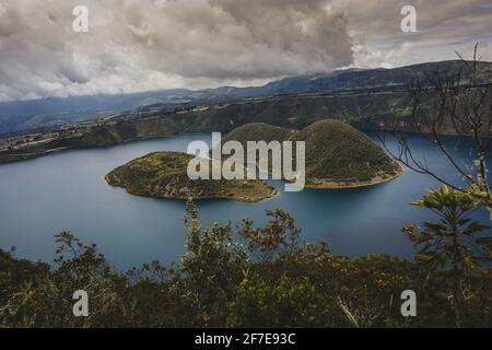 Blick auf die Insel am berühmten Cuicocha-See in Ecuador. Panorama über einen blauen See, umgeben von üppigem Grün und weißen Wolken. Stockfoto