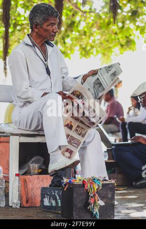 CARTAGENA, KOLUMBIEN, FEBRUAR 20 2017: Ein Schuhreiniger wartet auf den nächsten Kunden und liest eine Zeitung in der Nähe des Denkmals Torre del Reloj. Stockfoto