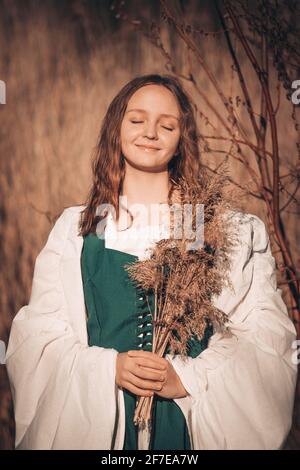 Glückliche mittelalterliche junge Frau in historischer Frauentracht mit Schilfstrauß an der Natur. Stockfoto