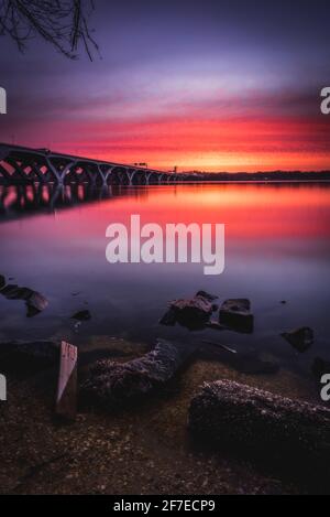 Sonnenaufgang am Ufer des Potomac River in Alexandria mit der Woodrow Wilson Bridge, die den Fluss in Maryland überspannt. Stockfoto