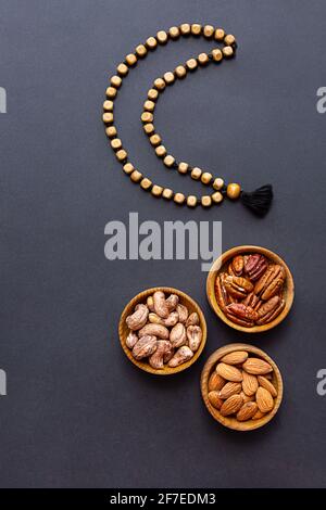Ramadan Kareem und iftar muslimisches Essen, modernes Urlaubskonzept. Holzschalen mit Nüssen und getrockneten Früchten und der Mond aus Perlen Stockfoto