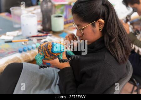 Junge mexikanische Frau handgemalt eine geschnitzte hölzerne Leguan Skulptur bekannt als alebrijes, San Martin Tilcajete, Oaxaca Staat, Mexiko. Stockfoto