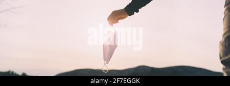 Die Coronavirus-Pandemie ist vorbei - lassen Sie die chirurgische Gesichtsmaske los. Hand hält medizinische psa Abdeckung draußen im Frühjahr Sonne Banner Panorama Stockfoto