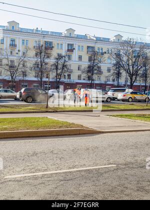 Moskau. Russland. 06. April 2021. Orangefarbene uniformierte Hausmeister, die auf einer Straße in der Stadt den Rasen fegen. Sonniger Frühlingstag. Die Arbeit der Gemeinde Stockfoto