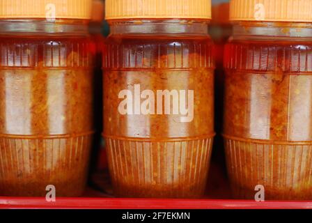 Kleine Plastikgläser voller hausgemachtes Chilliöl zum Verkauf. Das Bild zeigt rote und gelbe Farben. Stockfoto