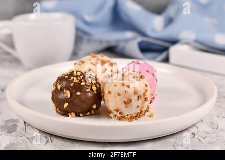 Bunte kleine Kuchenkugeln glasiert mit weißer, rosa und brauner Schokolade mit Streuseln auf weißem Teller Stockfoto