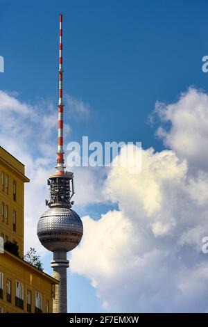 Springbrunnen mit sauberem Wasser am Strausberger Platz in der Nähe eines gelben Hochhauses und eines Fernsehturms am sonnigen Tag in Berlin. Stockfoto