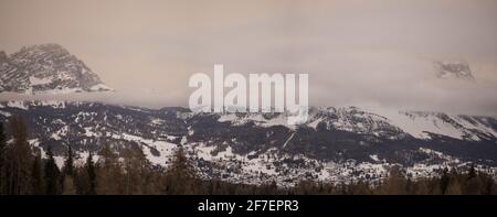 Winterpanorama von Cortina d'Ampezzo an kalten und bewölkten Tagen mit sichtbarer Stadt im Hintergrund. Geschichtete Wolken zwischen den Bergen. Stockfoto