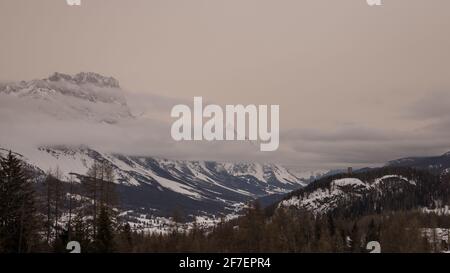 Winterpanorama von Cortina d'Ampezzo an kalten und bewölkten Tagen mit sichtbarer Stadt im Hintergrund. Geschichtete Wolken zwischen den Bergen. Stockfoto