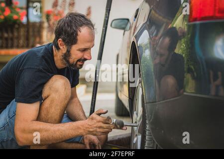 Seitenansicht eines kaukasischen Mannes, der ein modernes Autorad mit einer Ratsche abschraubt. Service eines Autos, Reifen- oder Radwechsel zu Hause. Stockfoto