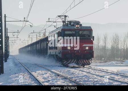 Ein Zug, der auf einer verschneiten Strecke auf die Kamera zufährt und Schnee vom Boden aufsteigt. Stockfoto