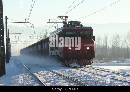 Ein Zug, der auf einer verschneiten Strecke auf die Kamera zufährt und Schnee vom Boden aufsteigt. Stockfoto