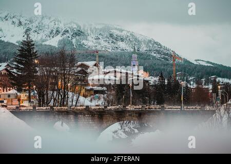 Am frühen Abend Panorama von Cortina d'Ampezzo loking von Westen in Richtung der Stadt und dem Glockenturm. Brücke über den Fluss im Vordergrund. Stockfoto