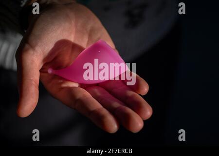 Menstruationstasse oder Menstruationstasse in rosa Farbe, die auf einer Hand einer Frau ruht. Moderne und modische Art der Menstruationsblutsammler. Stockfoto