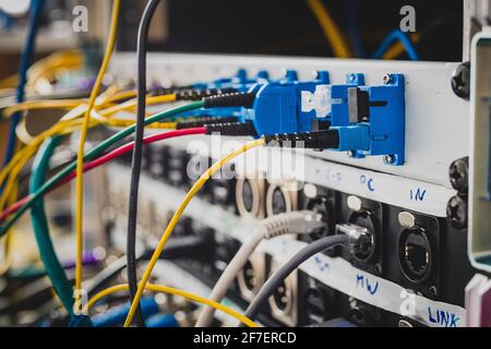 Verschiedene BNC-SDI-UTP- und optische Signalkabel, die auf der Rückseite eines Patchpanels eingesteckt sind. Eine Unordnung von Kabeln, die hinter dem Rack oder der Verkleidung sichtbar sind. Konzentrieren Sie sich auf die Stockfoto